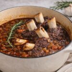 Braised chuck roast riblets in a Dutch oven with red wine sauce, carrots, onions and rosemary