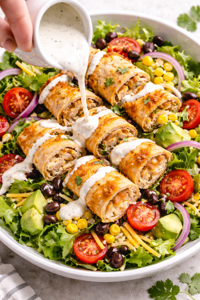 Chicken taquitos cut into pieces over a fresh salad with ranch dressing drizzled on top