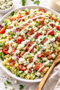 Chopped wedge pasta salad with elbow macaroni, romaine lettuce, crispy bacon, cherry tomatoes, blue cheese, and creamy wedge dressing in a white bowl.