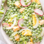 Classic pea and cheese salad made with green peas, cheddar cheese, hard-boiled eggs, celery, and radishes in a creamy dressing, served in a light bowl.