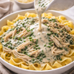 Shredded crockpot Boursin spinach chicken served over egg noodles with creamy sauce being poured on top