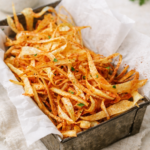 Crispy baked parsnip fries served in a rustic metal tray lined with parchment paper on a light linen background
