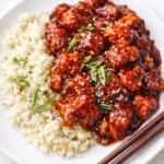 Crockpot bourbon chicken coated in a thick glossy sauce served over cauliflower rice with scallions and sesame seeds
