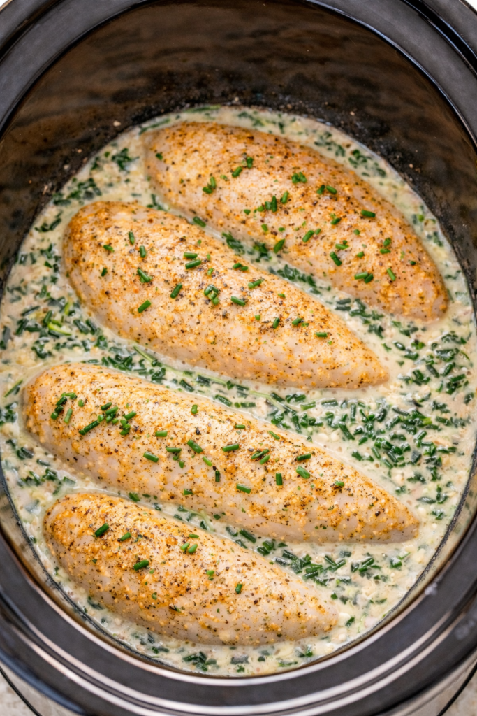 Creamy Boursin spinach chicken cooking in a crockpot with tender chicken breasts in a white wine cream sauce