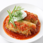 Plated crockpot stuffed cabbage rolls with tomato sauce and sour cream