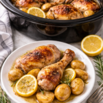 Easy crockpot honey lemon chicken with garlic and rosemary served on a plate with potatoes, shown in front of a slow cooker.