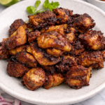Close-up of crispy slow cooker carnitas on a light ceramic plate with caramelized edges on a marble background.