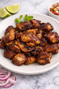 Close-up of crispy slow cooker carnitas on a light ceramic plate with caramelized edges on a marble background.
