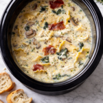 Creamy white lasagna soup with prosciutto, spinach, mushrooms, and lasagna noodles in a slow cooker on a marble background