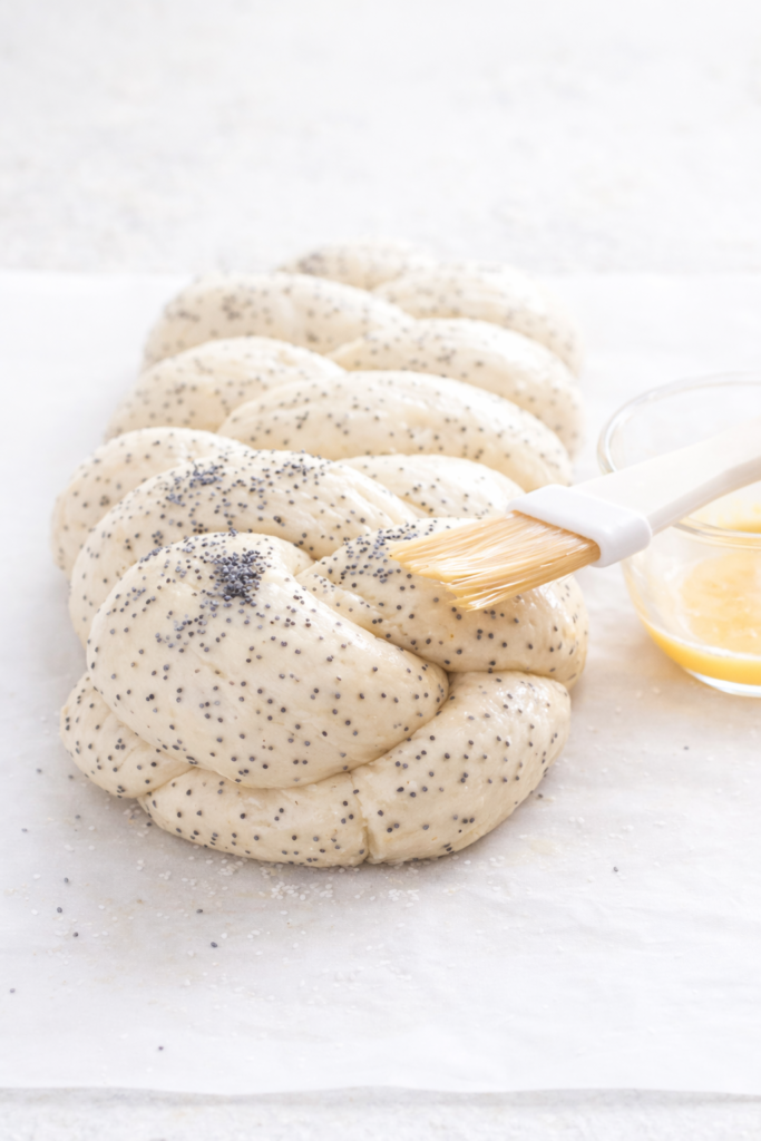 Brushing egg wash onto braided poppy seed bread dough before baking