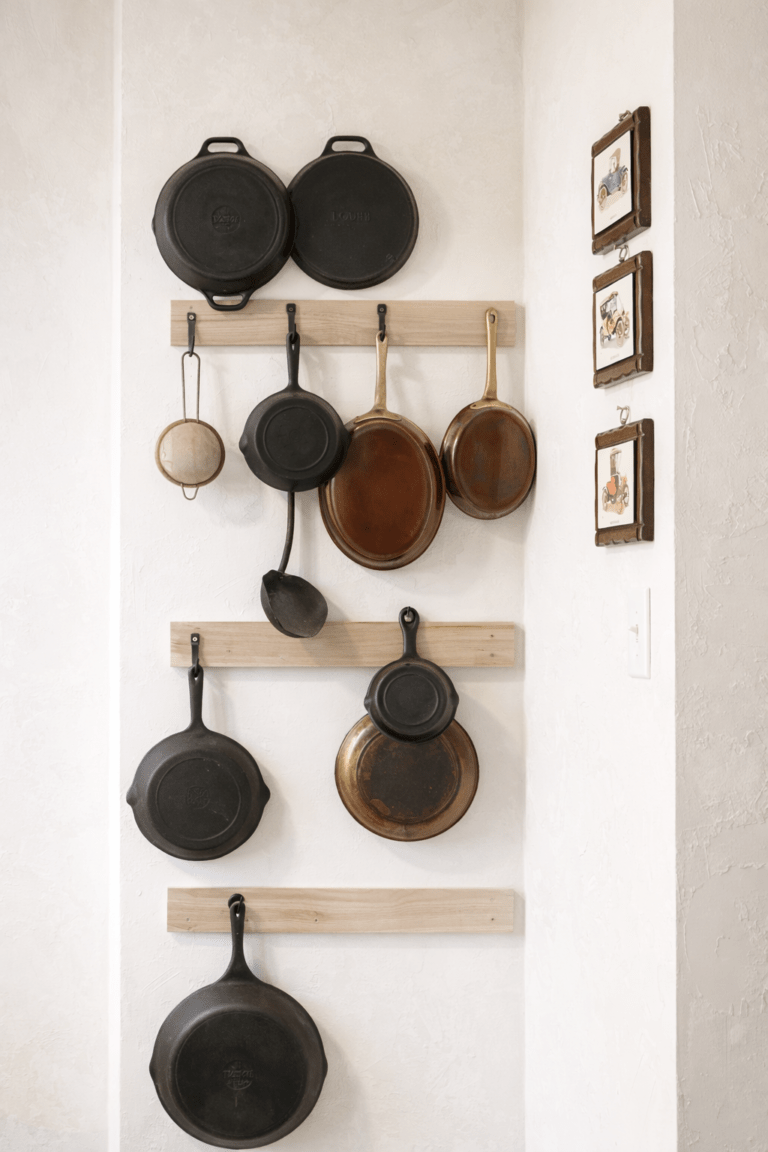 Farmhouse kitchen cast iron pan wall storage with wooden rails displaying cast iron and copper skillets in a vertical wall arrangement.