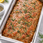 Greek chicken meatloaf baked in a loaf pan, golden brown and topped with fresh herbs, ready to slice and serve.