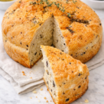 Greek olive and feta bread loaf sliced on marble surface with herbs and olive oil