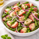 Classic green bean and potato salad made with red potatoes, fresh green beans, and red onion in a white serving bowl on a marble countertop.
