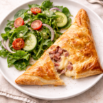 Flaky ham and cheese hand pie with a gooey, melty cheese center served on a white plate with a simple green salad.