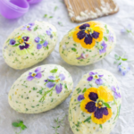 Herb and edible flower butter shaped like Easter eggs using plastic eggs, styled on parchment paper with an open purple plastic Easter egg in the background.