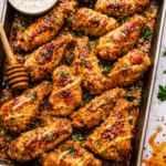 Overhead view of baked hot honey Dijon garlic chicken wings on a sheet pan with honey mustard drizzle and red pepper flakes