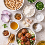 Flat lay of ingredients for hot honey falafel including chickpeas, fresh herbs, garlic, onion, spices, flour, honey, and hot sauce
