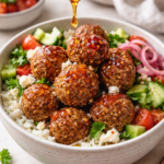Hot honey falafel rice bowl with crispy falafel being drizzled with spicy honey over rice, cucumbers, tomatoes, and feta