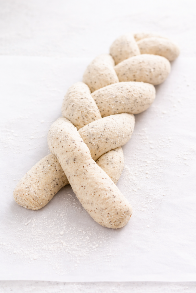 Braided poppy seed bread dough being shaped on a lightly floured surface before baking