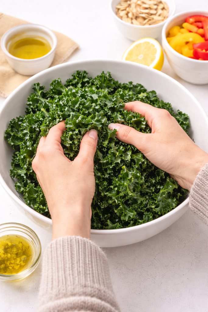 Hands massaging fresh kale in a white bowl with olive oil to soften leaves for an easy kale salad recipe