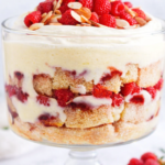 Irish sherry trifle layered with sponge cake, vanilla custard, raspberries, whipped cream, and toasted almonds in a clear glass trifle bowl.