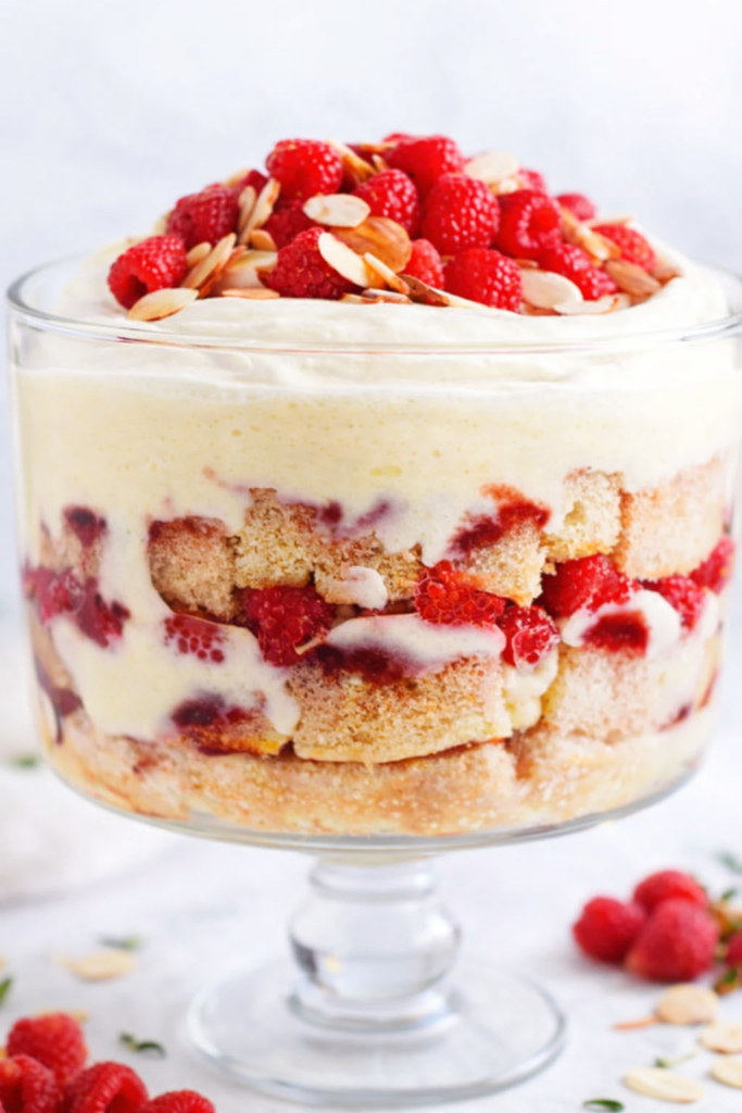 Irish sherry trifle layered with sponge cake, vanilla custard, raspberries, whipped cream, and toasted almonds in a clear glass trifle bowl.