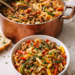 Italian drunken noodles cooked in a copper pot with a bowl of noodles served in front, featuring Italian sausage, bell peppers, egg noodles, and tomato wine sauce.