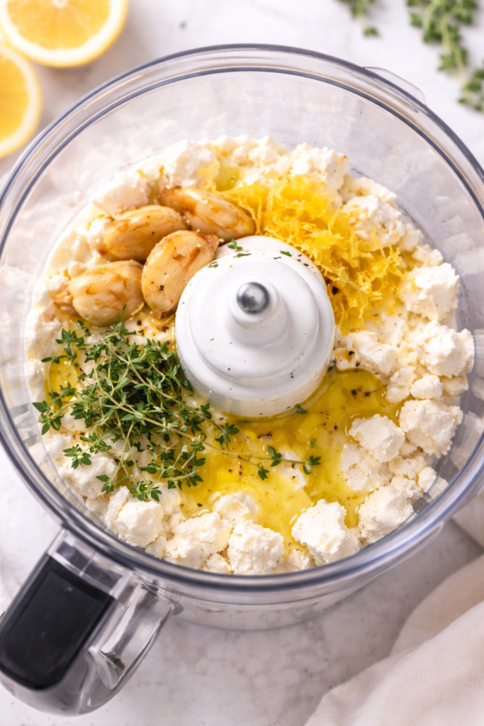 Roasted garlic, lemon zest, thyme and feta cheese in a food processor before blending into whipped feta dip.