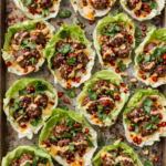 Mini Asian meatball lettuce cups drizzled with sriracha mayo and chili crisp on a rustic baking sheet