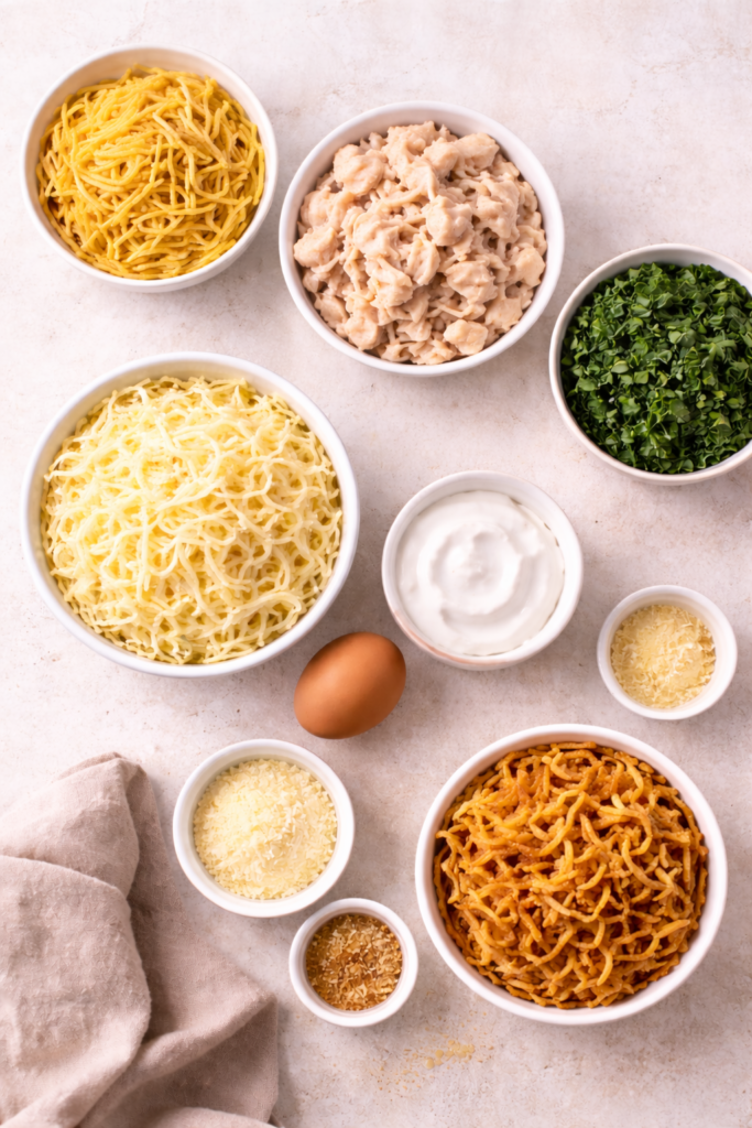 Flat lay of ingredients for Monterey chicken spaghetti bake including rotisserie chicken, spaghetti, cheese, spinach, sour cream, egg, and fried onions