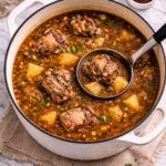Old-fashioned oxtail soup simmering in a white enameled cast iron Dutch oven with a ladle on a marble counter