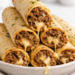 Oven baked cheesy ground beef taquitos stacked on a plate with melted cheese dripping from the center, golden tortillas, and a light bright background.