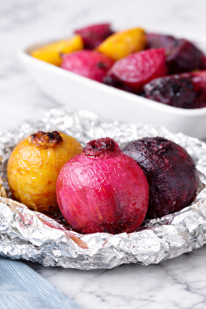 Oven roasted multicolor beets with golden, pink, and red beets resting on foil over a white marble surface