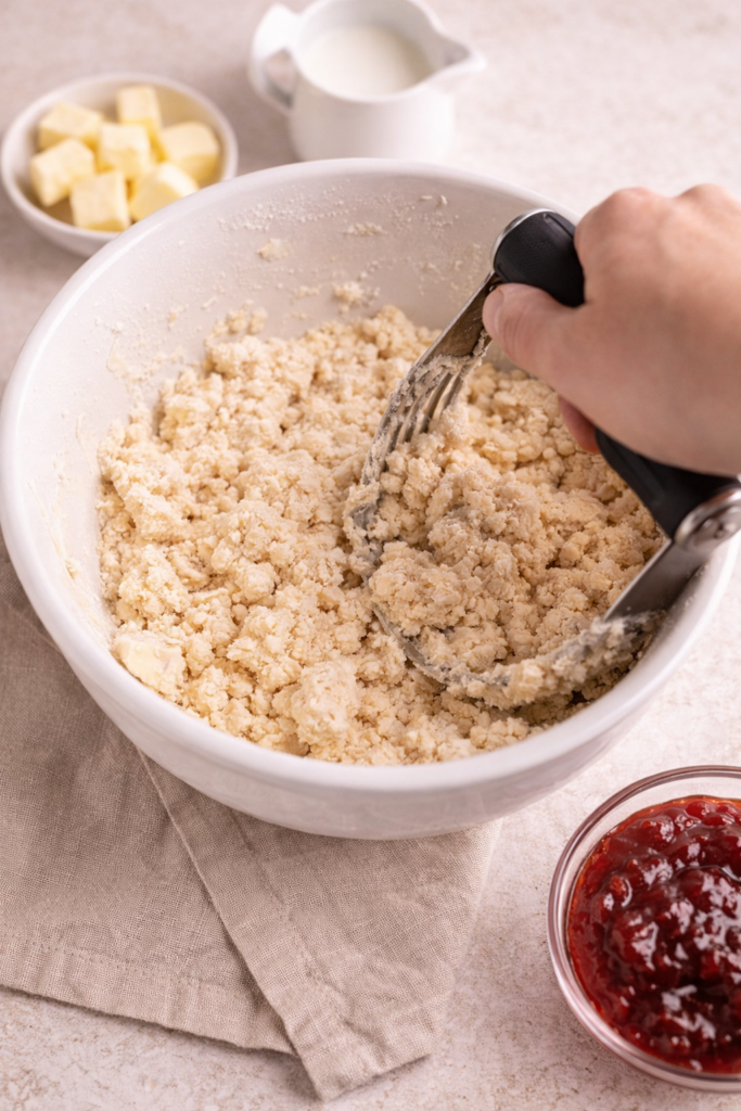 Peanut butter and jelly monkey biscuit dough being mixed in a white bowl with cold butter and flour