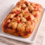 Peanut butter and jelly monkey biscuits baked in a loaf pan and served on a neutral ceramic plate with soft linen background