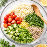 All ingredients for riced cauliflower tabbouleh arranged in a large glass mixing bowl with a wooden spoon on a marble countertop.