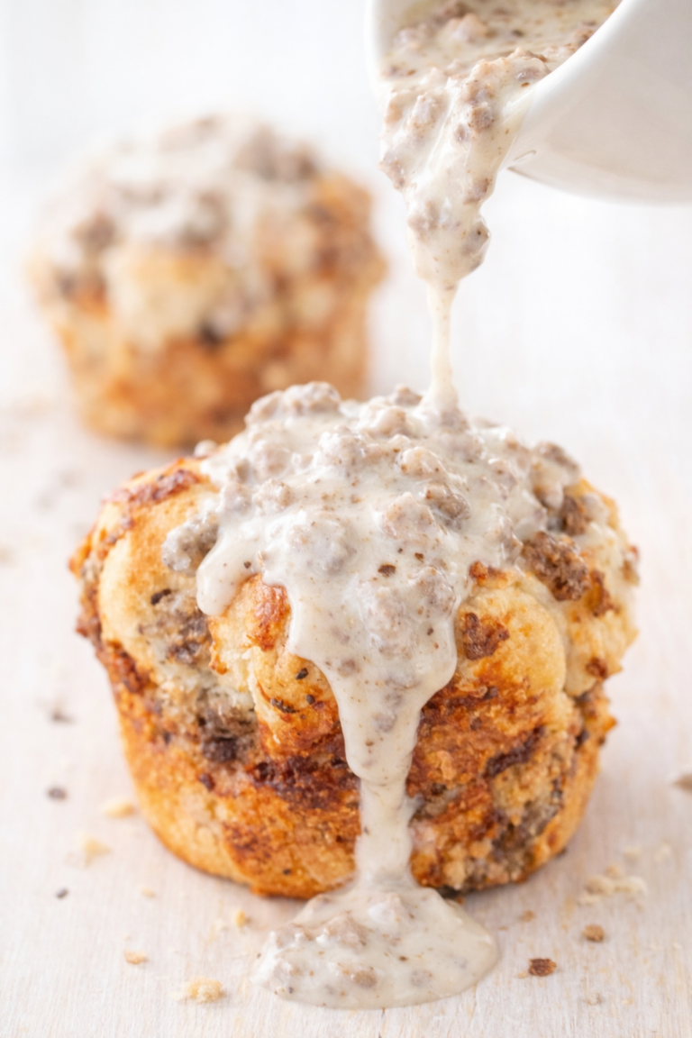 Light and fluffy breakfast sausage monkey muffin made with biscuit dough and cheese, topped with creamy sausage gravy being poured over the top.
