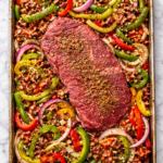 Raw flank steak and seasoned bell peppers, onions, and chorizo arranged on a sheet pan before cooking