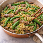 Sirloin snap pea stir fry with ramen noodles cooking in a copper skillet on a marble countertop, garnished with green onions.