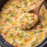 Creamy slow cooker green chile rice casserole finished in the crockpot with a spoon scooping out a cheesy serving.