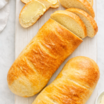 Light and bright homemade sourdough French bread loaves with a golden crust, sliced and served on a white board with butter, bakery-style and rustic.