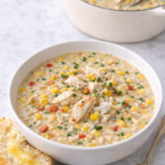 Bowl of creamy spicy Cajun corn and crab soup served with crusty bread and melted butter, with the soup pot in the background.