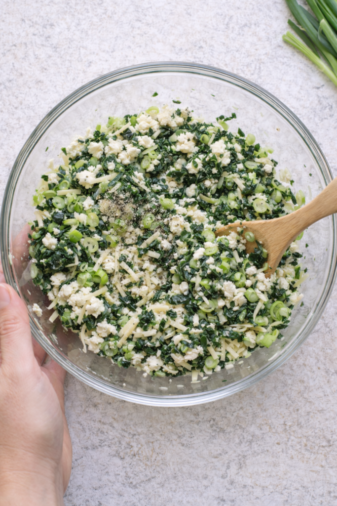 Spinach feta filling being mixed in a glass bowl for Greek spinach cheese rolls