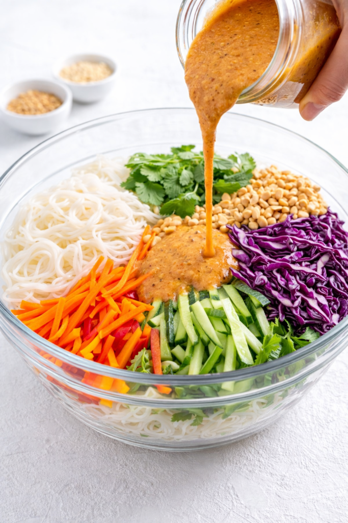 spring roll in a bowl salad in a glass bowl with ginger dressing being poured over rice noodles and fresh vegetables