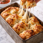 Hand pulling apart a cheesy bubble loaf made with biscuit dough, showing a gooey cheese pull in a rustic metal loaf pan on a marble countertop.