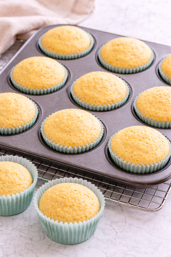 Freshly baked vanilla cupcakes cooling in a muffin pan on a light marble countertop