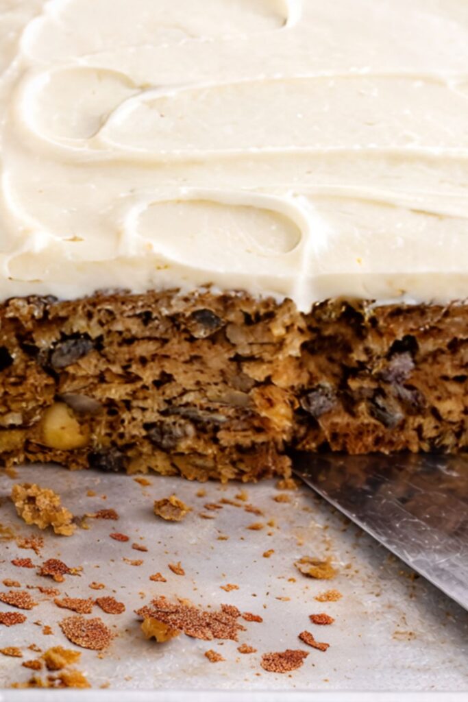 old fashioned applesauce spice cake with cream cheese frosting in a baking pan with one square missing and crumbs showing moist cake with walnuts and raisins