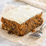 slice of old fashioned applesauce spice cake with cream cheese frosting on wrinkled parchment paper over a marble countertop