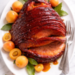 apricot molasses glazed ham on white platter with fresh apricots and glossy sticky glaze on marble countertop